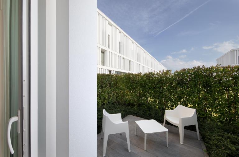 Terrazza con sedie bianche, tavolino e siepe verde.